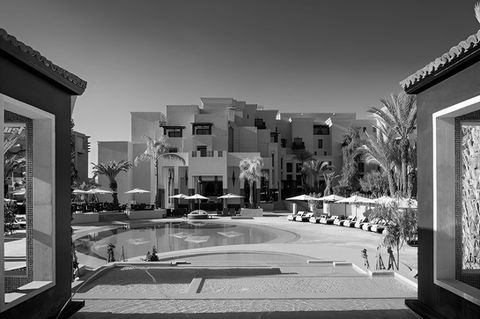 outdoor image of kempinski hotel in marrakesh, morocco, in traditioal clay architectural style with a contemporary pool