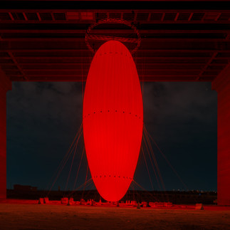 SpY’s OVOID (2024) is a site-specific installation composed of an illuminated egg-shaped structure suspended over a body of water, which challenges our perception of scale, space and movement. The newly commissioned artwork evokes the primordial form of the egg in its geometry, symbolizing the first place of refuge where life begins and maternal love manifests in its purest form.  Anchored to a bridge near Wadi Hanifah Dam, the 35-meter-high monumental ovoid looms above the lake. It emits a soft red glow from within, pulsing alternately to mirror the steady rhythm of life. From afar, the illuminated structure appears to multiply as it casts reflections on the water below.  This optical illusion invites the curious public to reflect on how our identity is always being shaped by the flow of life.