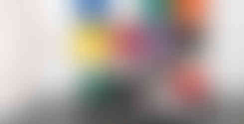 Matthias de Vogel aka artis fault lines lab sits in front of his colourful, primary colour woven contemporary canvas works in square forms next to a contemporary dining table