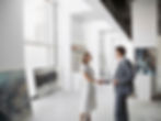 2 individuals shaking hands in business attire after negotiating a deal over purchasing an artwork, situated in an open contemporary gallery space