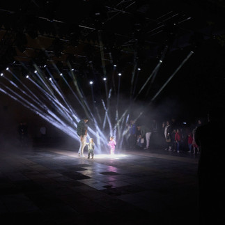 Random International’s Alone Together (2024) is an immersive installation that uses light beams to engage with the viewer in unexpected ways. Building on the collective’s previous artworks Audience (2008) and Living Room (2022), the piece delves into the fundamental contradiction at the heart of the human experience: the fear of being seen while longing for others to truly ‘see’ you.  The installation directs its moving lights on a visitor it selects at random, trailing them throughout the open-air arena at King Abdulaziz Historical Center. A custom tracking system gives the system a life of its own, allowing the beams to spotlight an individual based on various factors, sometimes acting unpredictably.  Illuminating one person at a time, the installation probes whether exposure empowers or renders us vulnerable. By inviting onlookers to co-create with the installation in an evolving and unpredictable interplay, Alone Together invites reflections on the ever-shifting relationship between loneliness and connection.