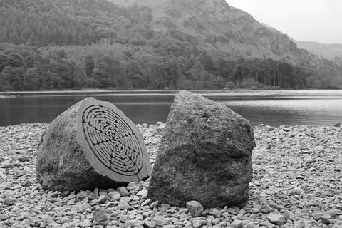 peter randall page's stone sculptures in organic forms and shapes located on a british lake in the beach area with trees as the backdrop