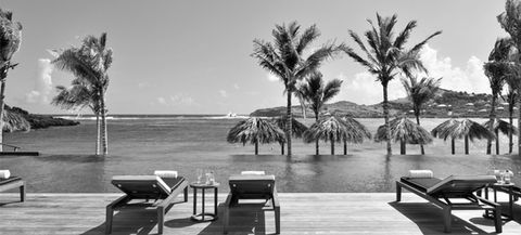 Photo credit to Key Hayden photography of a seychellois tropical beach in black and white featuring palm trees and contemporary deck chairs and an infinity pool