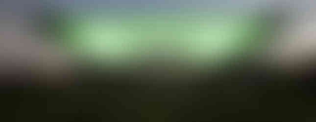 17. © Photo by Jared Opperman showing a green neon lit ceiling covering an open garden space with a path down the middle where a group of people are talking in a sunset lit photograph