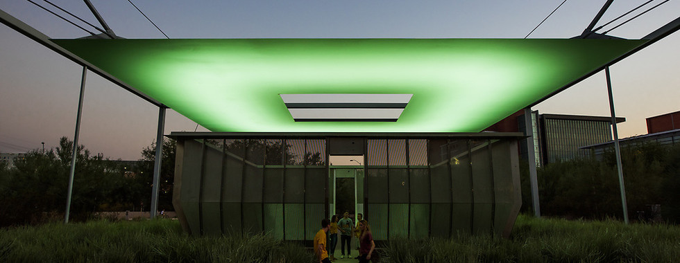 17. © Photo by Jared Opperman showing a green neon lit ceiling covering an open garden space with a path down the middle where a group of people are talking in a sunset lit photograph