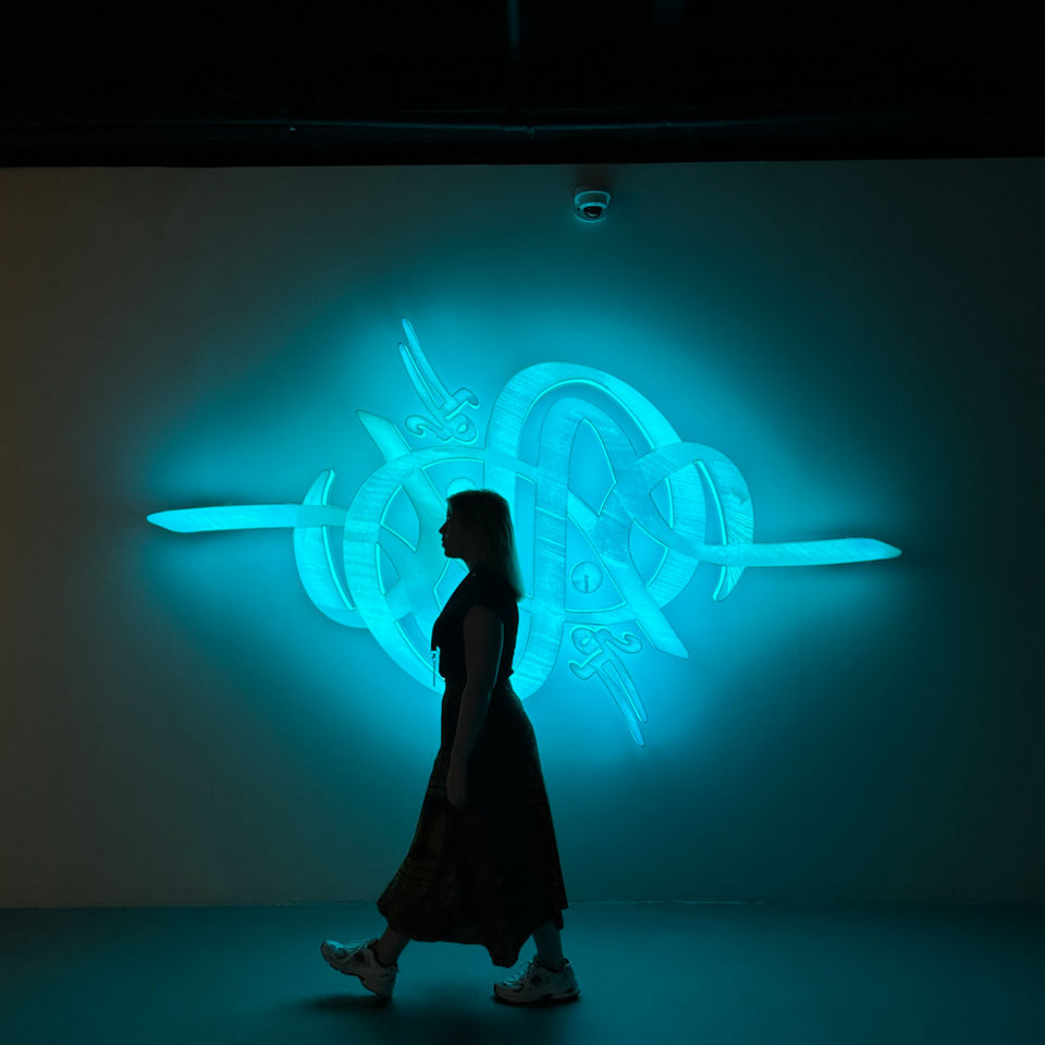 An artelier team member curator strolls past a contemporary calligraphic art installation at noor riyadh 2023 in blue fluorescent neon lighting
