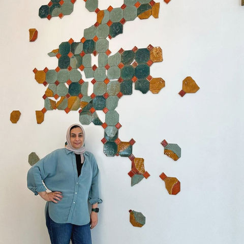 artist ghada, a ceramic artist based in manama, bahrain who is represented by uae-based art advisory artelier standing in front of her ceramic installation that can be found at raffles al areen palace, bahrain