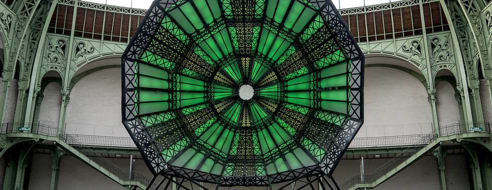 24. © Photo by Yann Caradec showing a huge circular green and black geometric metal art installation in the middle of a vintage european building with bright open glass ceiling inviting natural light