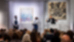 Sothebys auction with an audience bidding on an artwork held by two gallery specialists