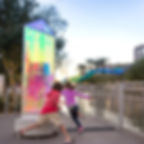 Artwork by Chris Wood in dichronic glass, light refracts through the pointed block creating colours of pink, green and blue, whilst children run around it playing 'It'.