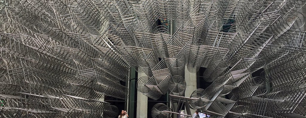 19. © Photo by Janette Asche showing thousands of silver metal bicycles stacked up on each other well above human height with a woman walking between them in a gap or an arch