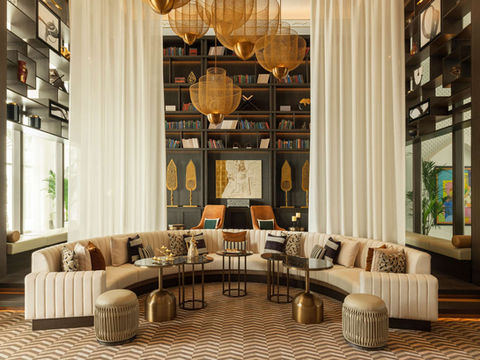 example of a luxury hotel project handled and managed by artelier's art curators, in raffles al areen palace bahrain. An artwork by ewan david eason, a gold leaf map artist managed under artelier art advisory, is at the centre of the lobby reception room / library, with large white drapes, a ceiling wall of books and a semi circular sofa .