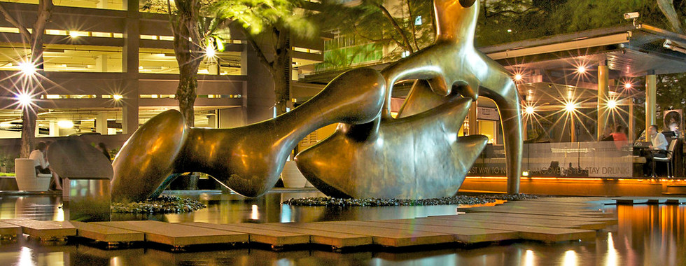 © Photo by William Cho of an abstract human figure made out of metal shot at night in an urban space as it sits above water with a stone slab bridge next to it