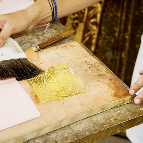Artist in their studio applying gold leaf with a large paintbrush
