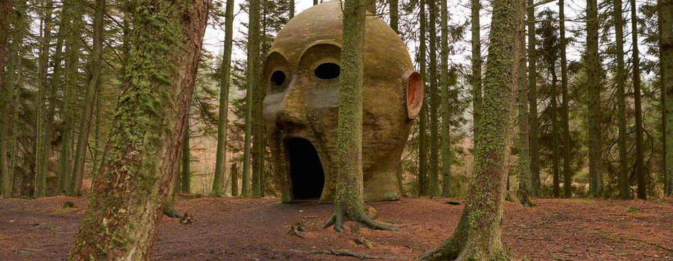 © Courtesy of Kielder art & architecture showing a large 3d head sculpture with its mouth open to the floor in the middle of a dense forest