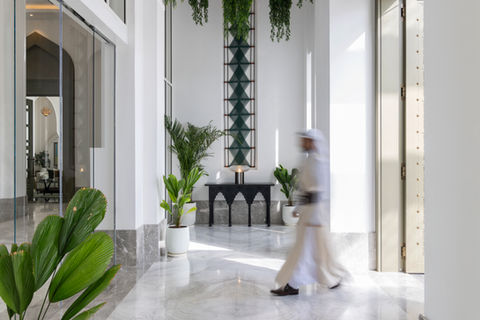 exemplar art work from artelier's art collection at raffles al areen palace, bahrain, featuring a bahraini man walking in a blurred motion in front of a woven green wall piece tapestry