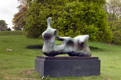 A collectable sculpture by henry moore in a british field with an oak tree and sheep in the background