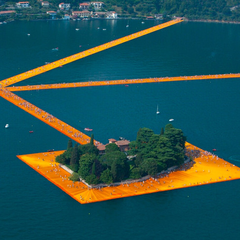 A large orange rectangular form with trees growing in the middle, as it appears to float on a body of water. It's orange lines connect its central form to the island in the background.