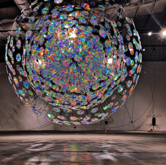 Jiyen Lee’s Stain-Rainbow Forest 2.3 (2023-2024) is a sculptural light installation created using 3D printing and nanopattern replication. Inspired by invisible patterns in nature, the newly commissioned artwork depicts instances when these natural phenomena become visible to the human eye through technology.  It is the latest iteration in Lee’s Stain-Rainbow Forest series, which serves as a metaphorical space for imperfect beings to coexist in. Visitors stroll through Lee’s forest composed of reflective discs hanging from the ceiling and fixed to the floor.  As the sculptures spin in the air, the nanofilm imprinted on them reflects a kaleidoscope of colors, effectively dousing the space and the viewer in fragmented rainbows. Though the forest glistens from afar, on closer inspection, its discs carry uniquely flawed patterns from the imprinting process, inspiring the viewer to see the beauty in the insignificant and ordinary.