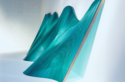 large glass transparent blue/green installation artwork set against a white wall.
