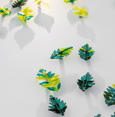 up close shot of artwork in the hallway located at raffles al areen palace in the entrance area featuring tall white walls and ceilings featuring a hand blown glass wall installation display featuring dozens of hand crafted glass leaves of different greens in tones, hues and textures