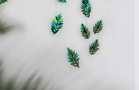 up close shot of artwork in the hallway located at raffles al areen palace in the entrance area featuring tall white walls and ceilings featuring a hand blown glass wall installation display featuring dozens of hand crafted glass leaves of different greens in tones, hues and textures