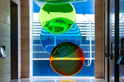 Window corridor next to elevators featuring a colourful trio of circular glass pane artworks by danny lane