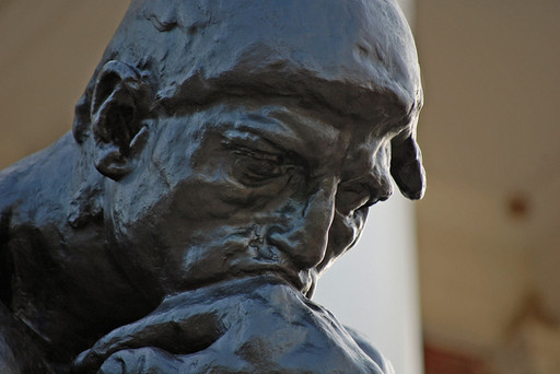 A close-up of Rodin's 'The Thinker' placed in outside as a public artwork, showcasing a detail of the bronze sculpture's face in contemplation.