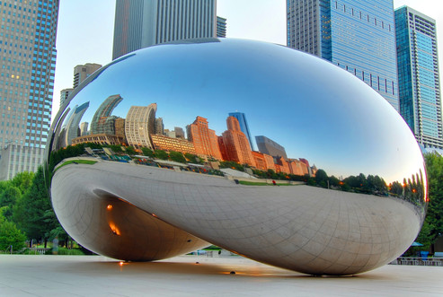 A closeup of 'Cloud Gate' by Anish Kapoor with the cityscape in sunset reflected on the large glass public artwork.