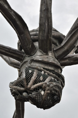 A close-up of Louise Bourgeois' 'Maman', showing the spindly steel body with metal netting, up close against a grey sky.
