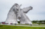 Large-scale outdoor public art sculptures, depicting two metal horseheads, one with their head forward and the other with their head tilted backwards.