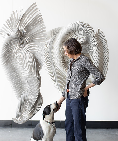 An image of kristy kun next to her artwork sculpture as she caresses her black and white dog