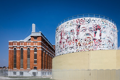 large scale billboard on watertank by vhils next to a period industrial building in red brick