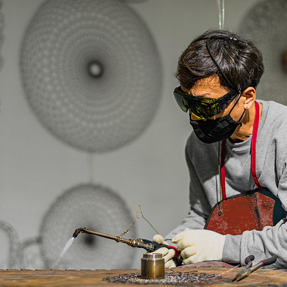 Artist firing metal in his studio with circular large scale metal artworks in the background in blurred aesthetic