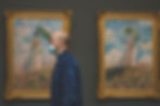 Person wearing a covid mask walking past some impressionist paintings in a museum space