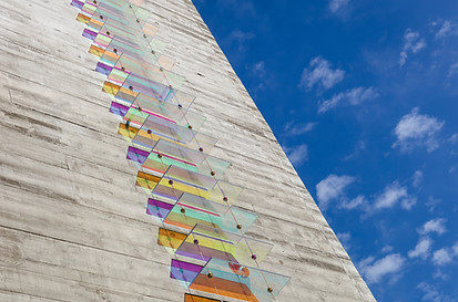 glass artwork set against an outdoor building, with a blue sky scenery in the right background