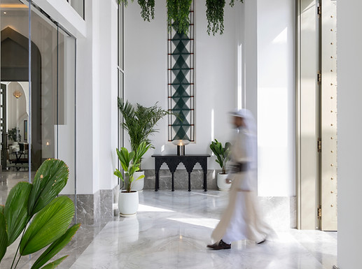 a bahraini man strolls in a blur towards the hotel lobby of raffles bahrain, with an artwork commissioned by artelier behind made out of geometric woven wall hanging in green thread