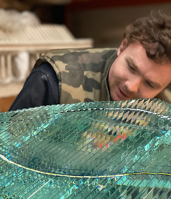 portrait of artist danny lane's workshop assistant looking and inspecting over a public art commission sculpture made of glass imitating wave like formations in turquoise blue