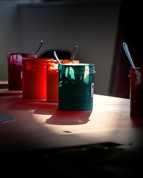 a scenic shot of green, orange and purple pots of paints with spoons in the pots located at a private art studio