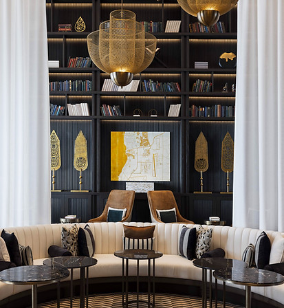 library within raffles bahrain hotel centrally shot face forwards,  located amongst a golden-leafed canvas artwork of bahrain's map alongside gold spears engraved with  arabic poetry.