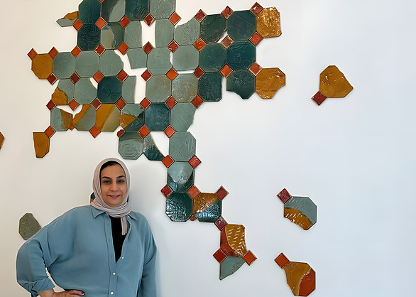 a portrait of ghada in front of her ceramic tile wall artwork for the raffles, bahrain project managed by artelier art consultancy 