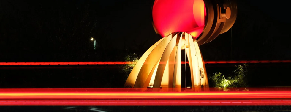 © Courtesy of North east statues showing a night lit photo of a large brightly lit sculpture showing a big red neon bucket pouring out artificial waves of yellow neon molten