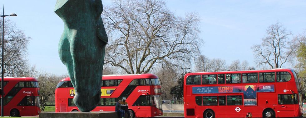 © Photo by Maggie Jones showing a huge horse head sculpture in London with three read london buses positioned behind it, to the right is a little girl in a red coat surrounded by pigeons