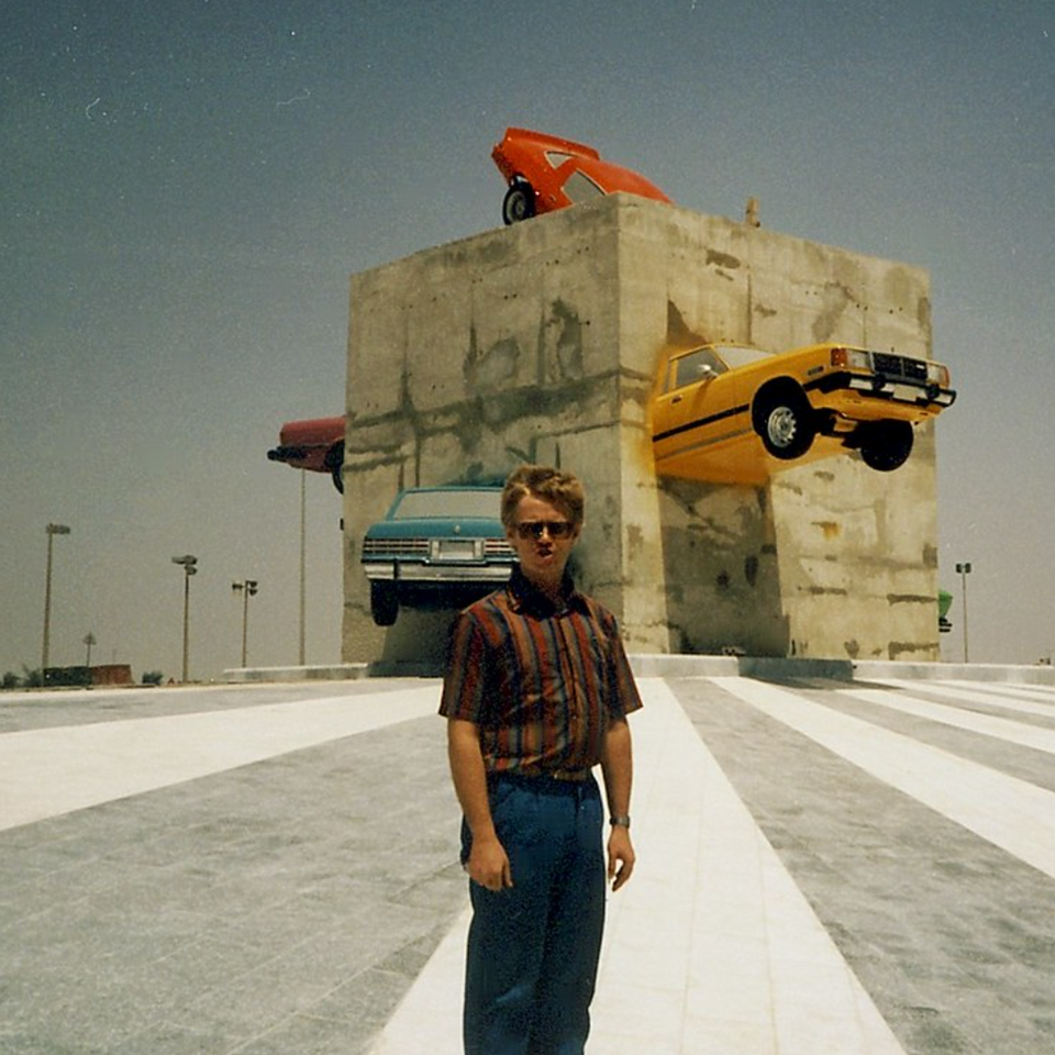 Contemporary public art installation featuring the portrait of a young child and a cemented block binding several colourful vintage cars in the background