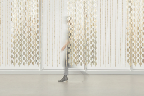 blurred woman walking behind an art exhibition run by artist and studio giles miller, featuring a gold metallic curtain of circles suspended from the ceiling